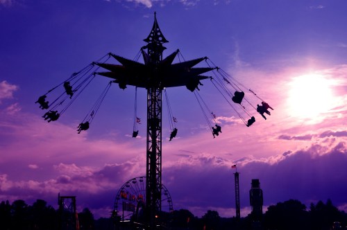 Silhouette of a swing ride against a vibrant purple sky with clouds and a setting sun.