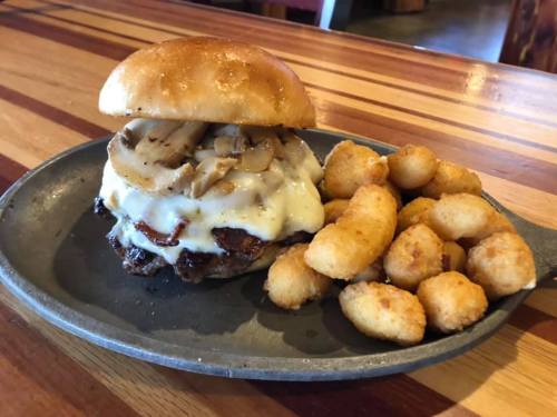 A juicy burger with melted cheese and grilled mushrooms, served with crispy tater tots on a metal plate.
