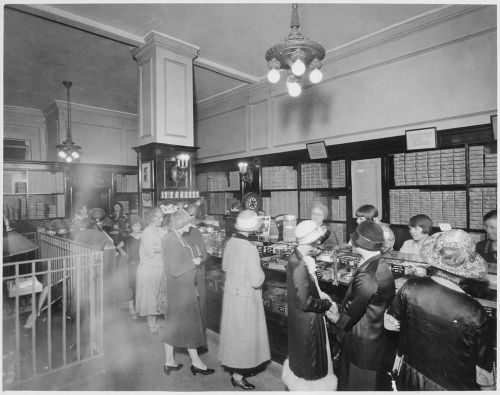 A vintage black-and-white photo of a busy store interior with women shopping and browsing products.