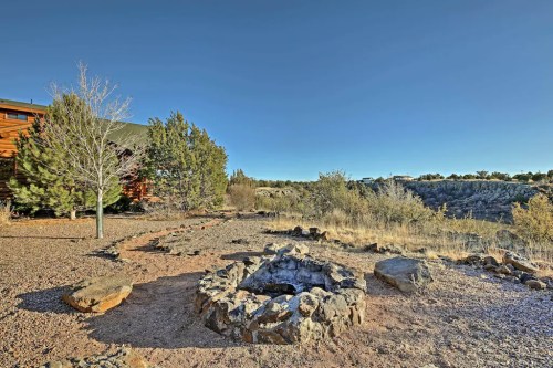 A rocky fire pit surrounded by sparse vegetation and trees, with a clear blue sky in the background.