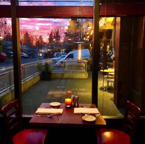 A cozy restaurant table set for two, with a beautiful sunset visible through large windows.