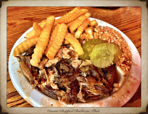 A plate of chopped barbecue with crinkle-cut fries, pickles, and a side of coleslaw.