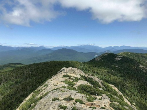 A panoramic view of mountains and lush green forests under a partly cloudy sky.