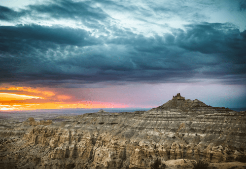 A dramatic sunset over rugged cliffs, with a distant castle-like structure silhouetted against colorful clouds.