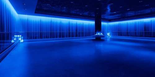 A dimly lit room with blue lighting, featuring curtains and illuminated objects on a central platform.