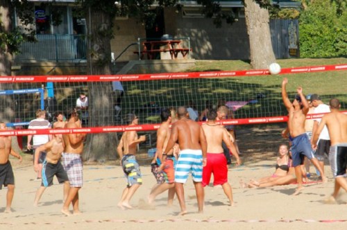 A lively beach volleyball game with players in swimwear, surrounded by spectators and a sunny outdoor setting.