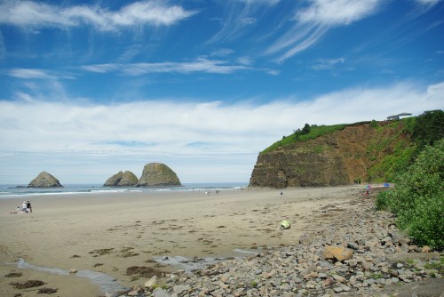 A scenic beach with rocky formations, cliffs, and a clear blue sky, featuring people enjoying the shoreline.