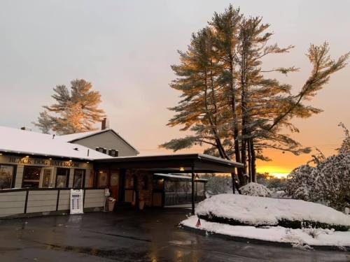 A snowy scene at Black Dog Ballroom, with trees and a sunset in the background.