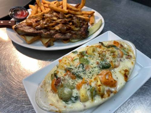 A plate of creamy baked pasta with vegetables and cheese, alongside a serving of fries and a meat dish.