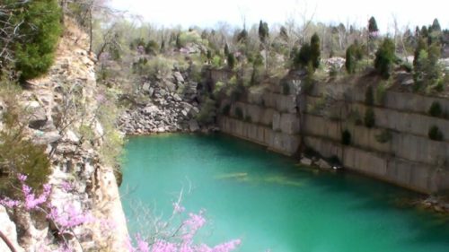 A serene turquoise quarry surrounded by rocky cliffs and greenery under a clear sky.