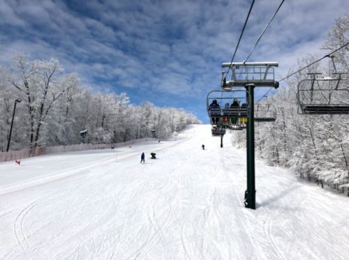 A snowy ski slope with a chairlift and skiers enjoying the winter scenery under a blue sky.