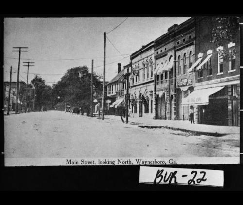 Black and white photo of Main Street in Waynesboro, GA, looking north, featuring storefronts and power lines.