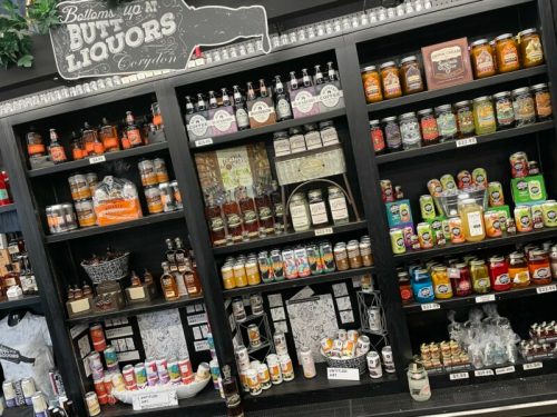 Shelves filled with various bottles of liquor, jars, and canned goods in a store display.