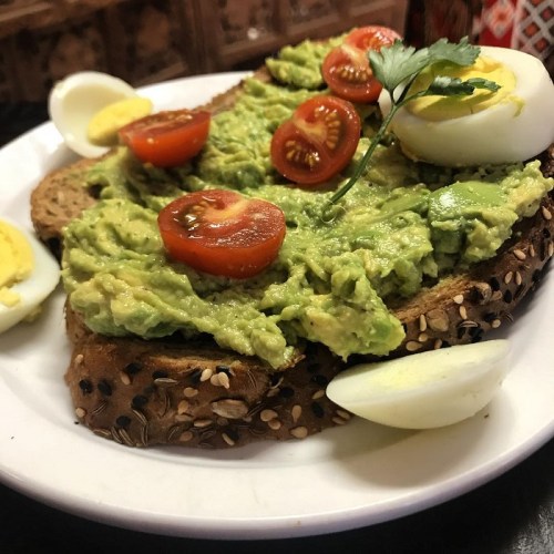 A plate of whole grain toast topped with mashed avocado, cherry tomatoes, and sliced hard-boiled eggs.