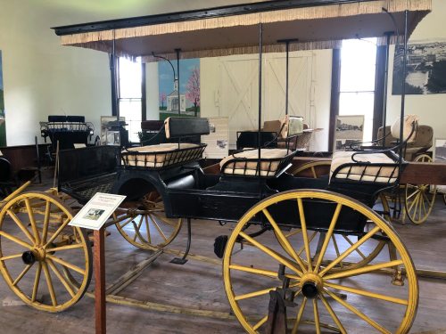 A vintage horse-drawn carriage with yellow wheels displayed in a museum setting.