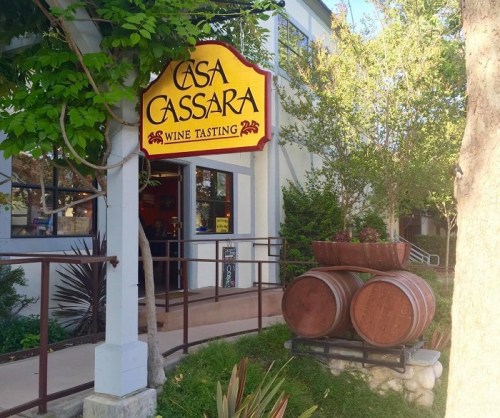 Sign for Casa Cassara Wine Tasting with wine barrels and greenery outside a building.