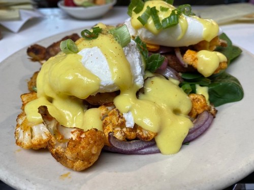 A plate of poached eggs on roasted cauliflower and spinach, topped with hollandaise sauce and green onions.