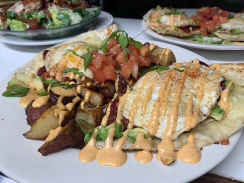 A plate of nachos topped with two fried eggs, diced tomatoes, green onions, and drizzled with a creamy sauce.