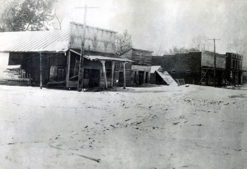 Black and white photo of a deserted town with wooden buildings, likely affected by flooding or a natural disaster.