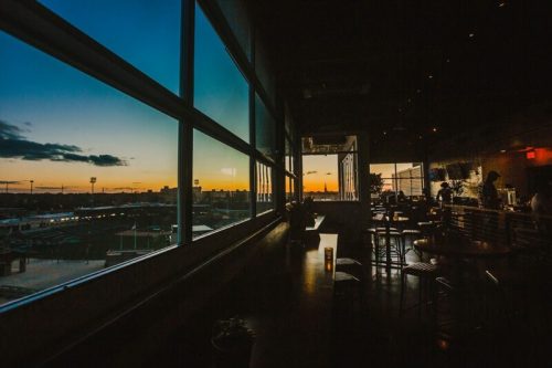 A cozy restaurant interior with large windows showcasing a vibrant sunset over the city skyline.