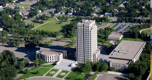 Aerial view of a tall government building surrounded by green spaces and parking lots in a suburban area.