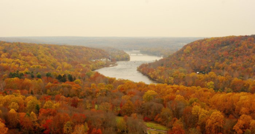 A scenic view of a river winding through vibrant autumn foliage in shades of orange, yellow, and red.
