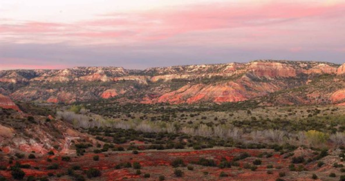Vast landscape featuring colorful rock formations and a sunset sky over a serene valley.
