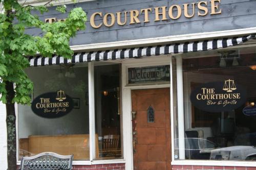 Exterior of The Courthouse Bar & Grille, featuring a wooden door and large windows with signage. Green tree in view.