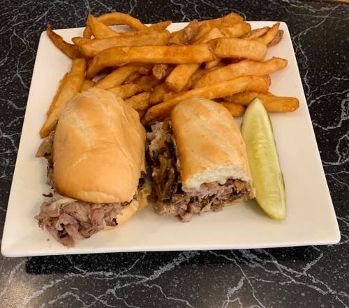 A plate with two sandwiches filled with shredded meat, served with crispy fries and a pickle on the side.