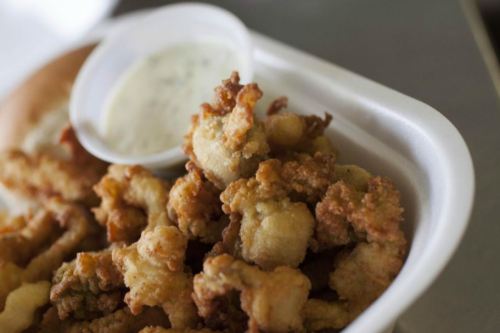 A takeout container filled with fried seafood, accompanied by a small cup of dipping sauce and a bun.