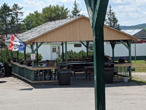 A covered outdoor seating area with picnic tables, surrounded by greenery and a flag flying in the breeze.