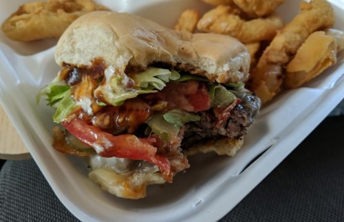 A close-up of a half-eaten burger with lettuce, tomato, and sauce, accompanied by crispy fries on a white tray.