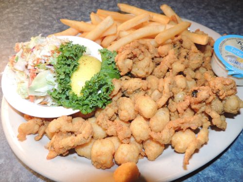 A plate of fried seafood, including small fried clams, French fries, a side salad, and a lemon wedge.