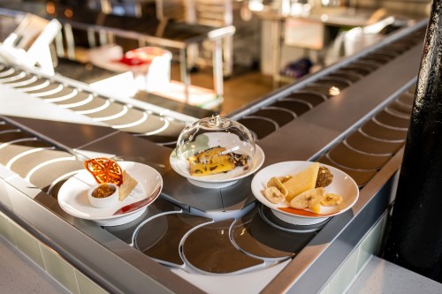 Three dessert plates on a counter: one with a tart, one under a glass dome, and another with assorted fruits.