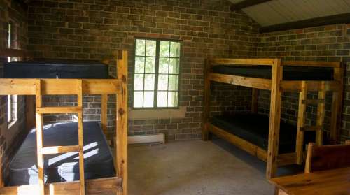 Interior of a rustic cabin with two sets of wooden bunk beds and a large window letting in natural light.