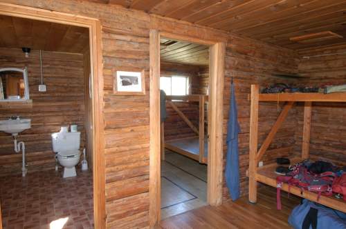 Interior of a rustic cabin featuring wooden walls, a bathroom area, and bunk beds.