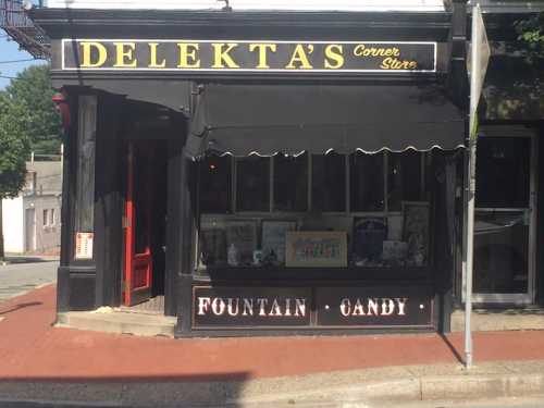 A corner store named "Delekta's" featuring a sign for fountain drinks and candy, with a classic storefront design.