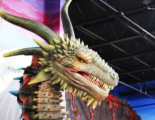 A detailed dragon head sculpture with sharp teeth and vibrant scales, set against a colorful background.