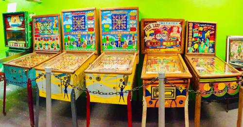 A row of vintage pinball machines with colorful designs against a bright green wall.