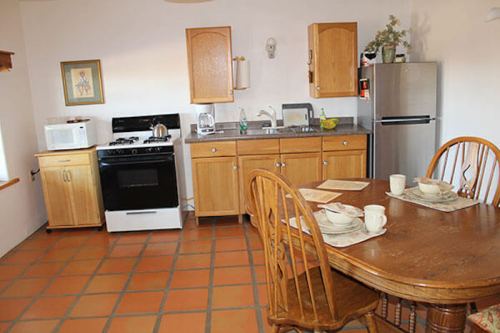 A cozy kitchen with wooden cabinets, a dining table set for four, and appliances including a stove and refrigerator.
