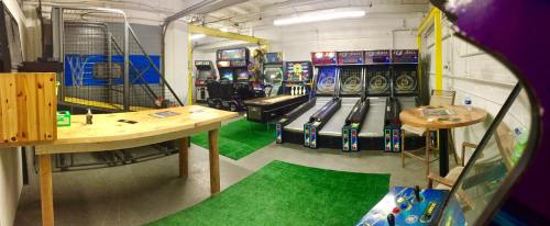 A retro arcade room featuring various games, including skee-ball and pinball machines, with a wooden table and green carpet.