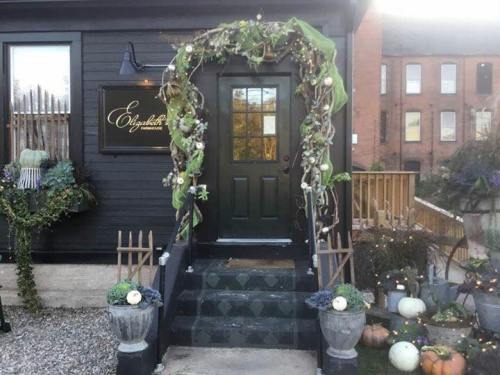 A black door adorned with a decorative green and floral arch, leading to a charming building with pumpkins nearby.