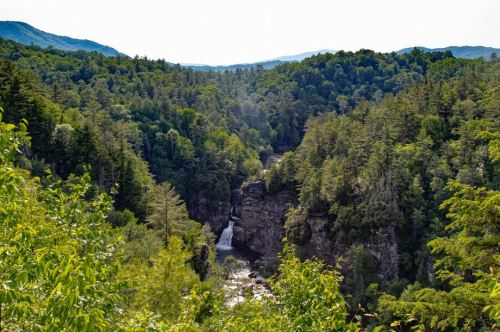 A scenic view of a lush green valley with a waterfall cascading through rocky cliffs, surrounded by mountains.