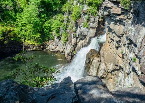 A waterfall cascading over rocky cliffs into a serene pool, surrounded by lush green trees.