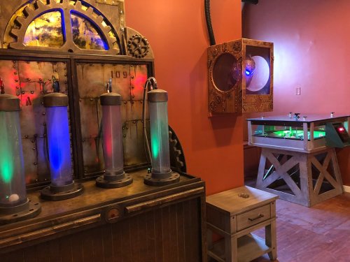 A steampunk-themed room featuring illuminated tubes and a control panel with colorful lights and gears.