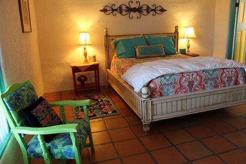 Cozy bedroom with a patterned bedspread, green chair, and warm lighting from bedside lamps.