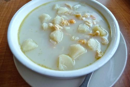 A bowl of creamy soup with chunks of potatoes and small pieces of chicken, served on a wooden table.