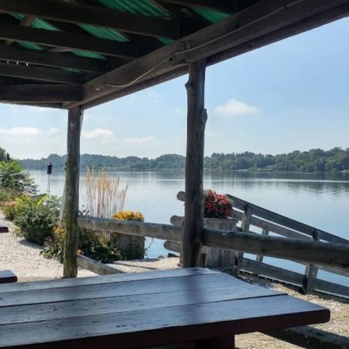 A serene view of a calm lake from a wooden gazebo, with flowers and greenery in the foreground.
