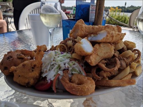 A plate piled high with fried seafood, including fish, shrimp, calamari, fries, and a side of coleslaw.