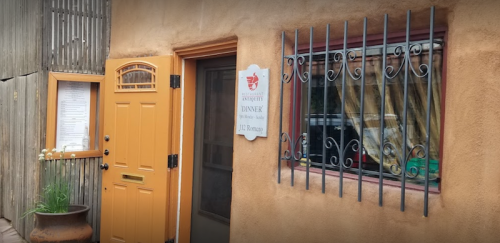 A rustic restaurant entrance with an orange door, window with bars, and a sign indicating dinner service.